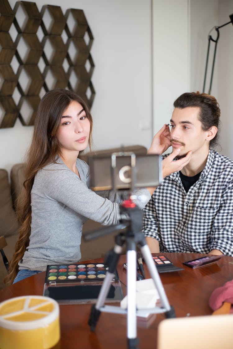 A Woman Applying Makeup On A Man's Face While Vlogging