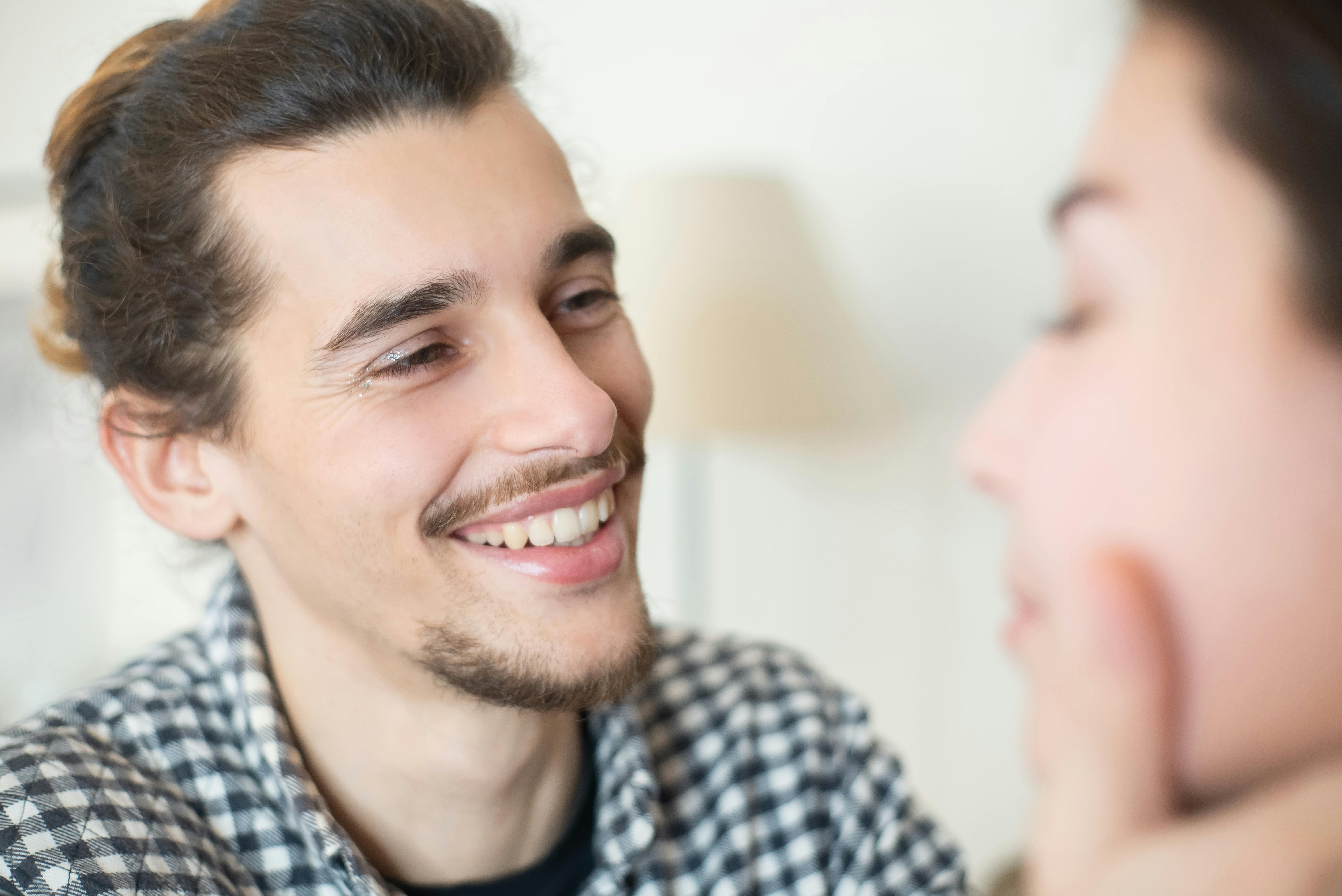 Cheerful bearded man smiling at a woman indoors, capturing a moment of happiness and connection.