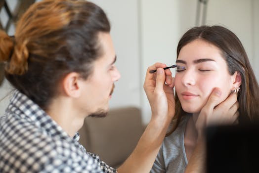 Close-up of a makeup artist applying eyeliner to a woman's eyes in a professional setting.