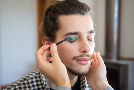 A makeup artist applies green eyeshadow to a male model indoors.