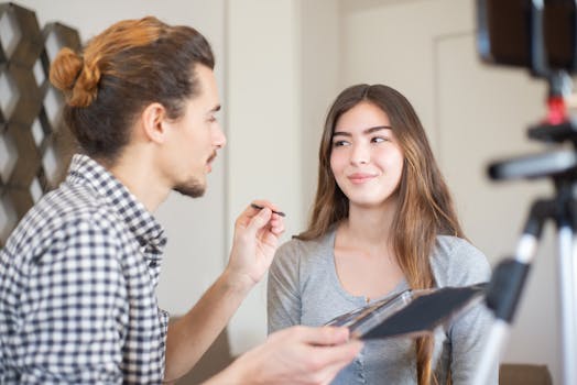 A makeup artist applies eyeshadow to a smiling woman during a vlog recording.