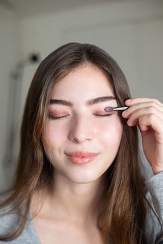 Close-up of a woman applying eyeshadow with a brush, eyes closed.