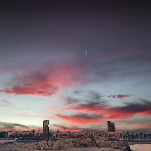 Scenic view of stone monuments under cloudy sky with crescent moon and stars at sundown in city