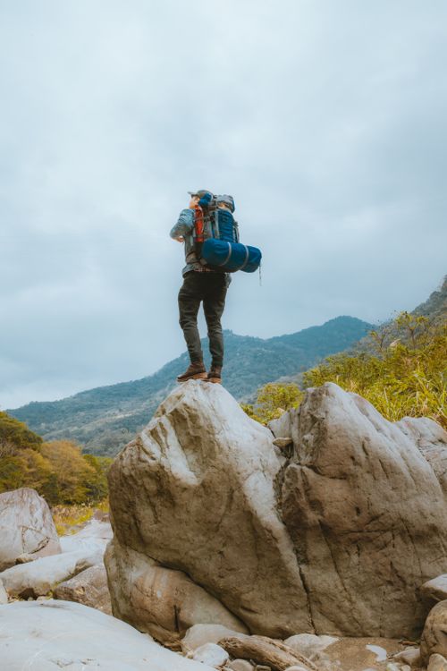 Free A male backpacker standing on large rocks, enjoying a mountain view. Stock Photo