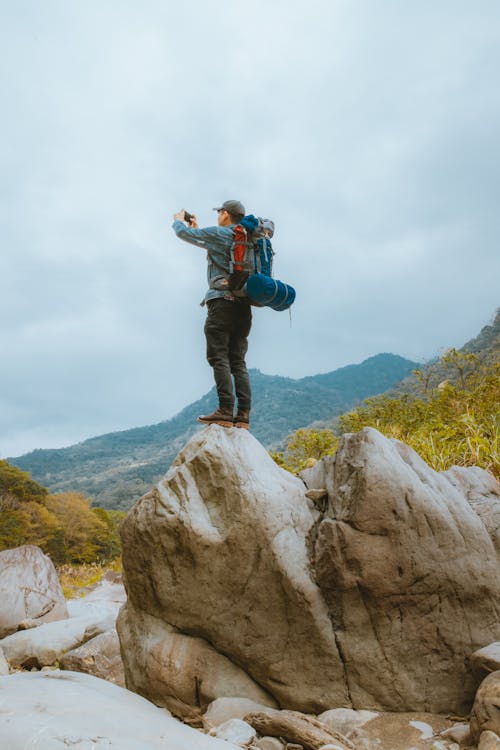 Backpacker Standing on Rock in Mountains and Photographing