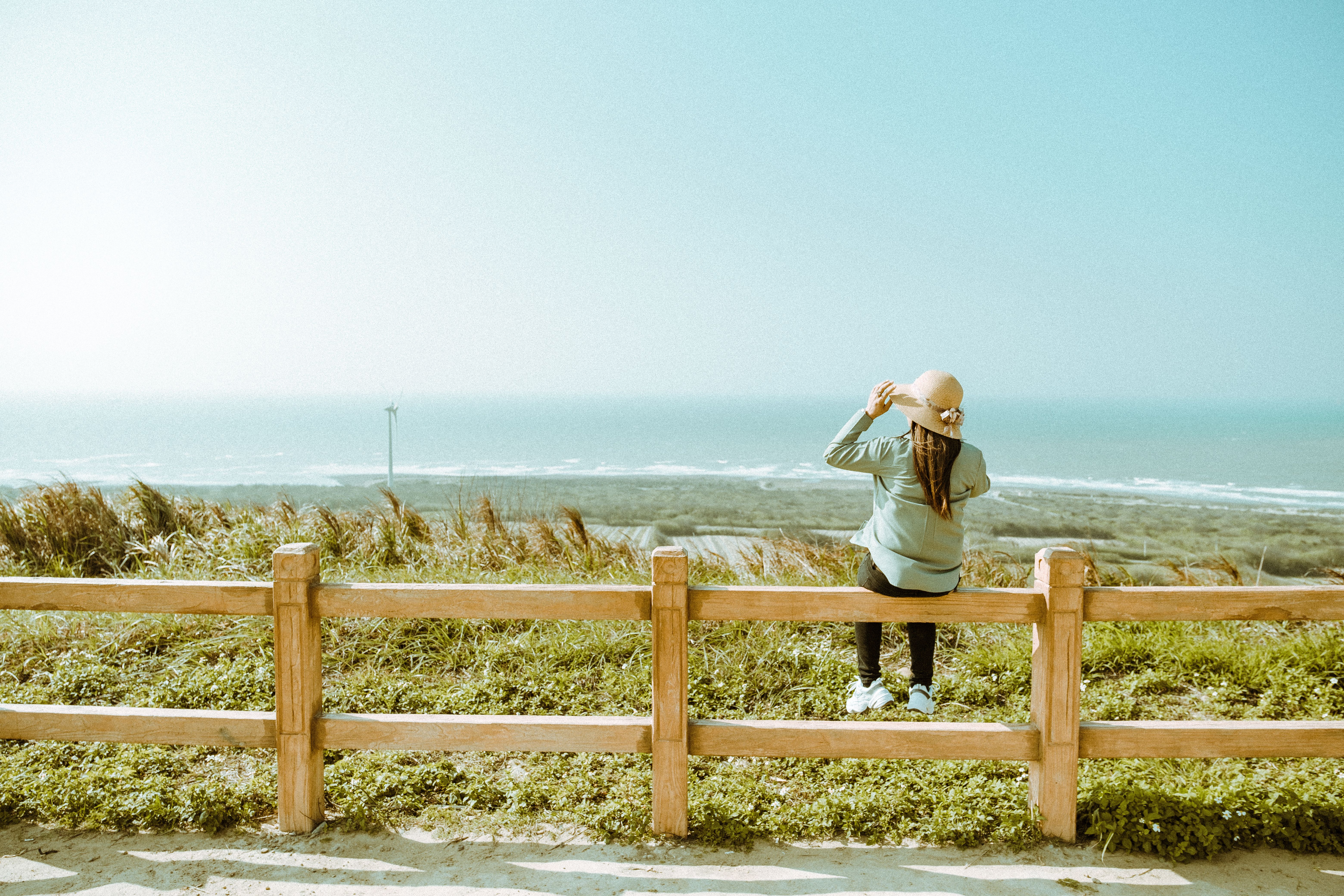 A woman in a hat gazes at the ocean horizon from a grassy coastal area, providing a sense of tranquility.