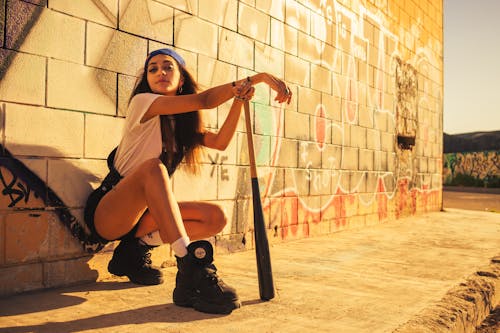 Photo of a Woman Crouching Near a Wall with Graffiti