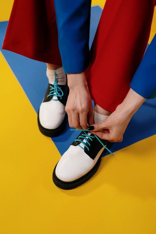 Free Close-up of hands tying shoelaces on stylish shoes against vibrant background. Stock Photo
