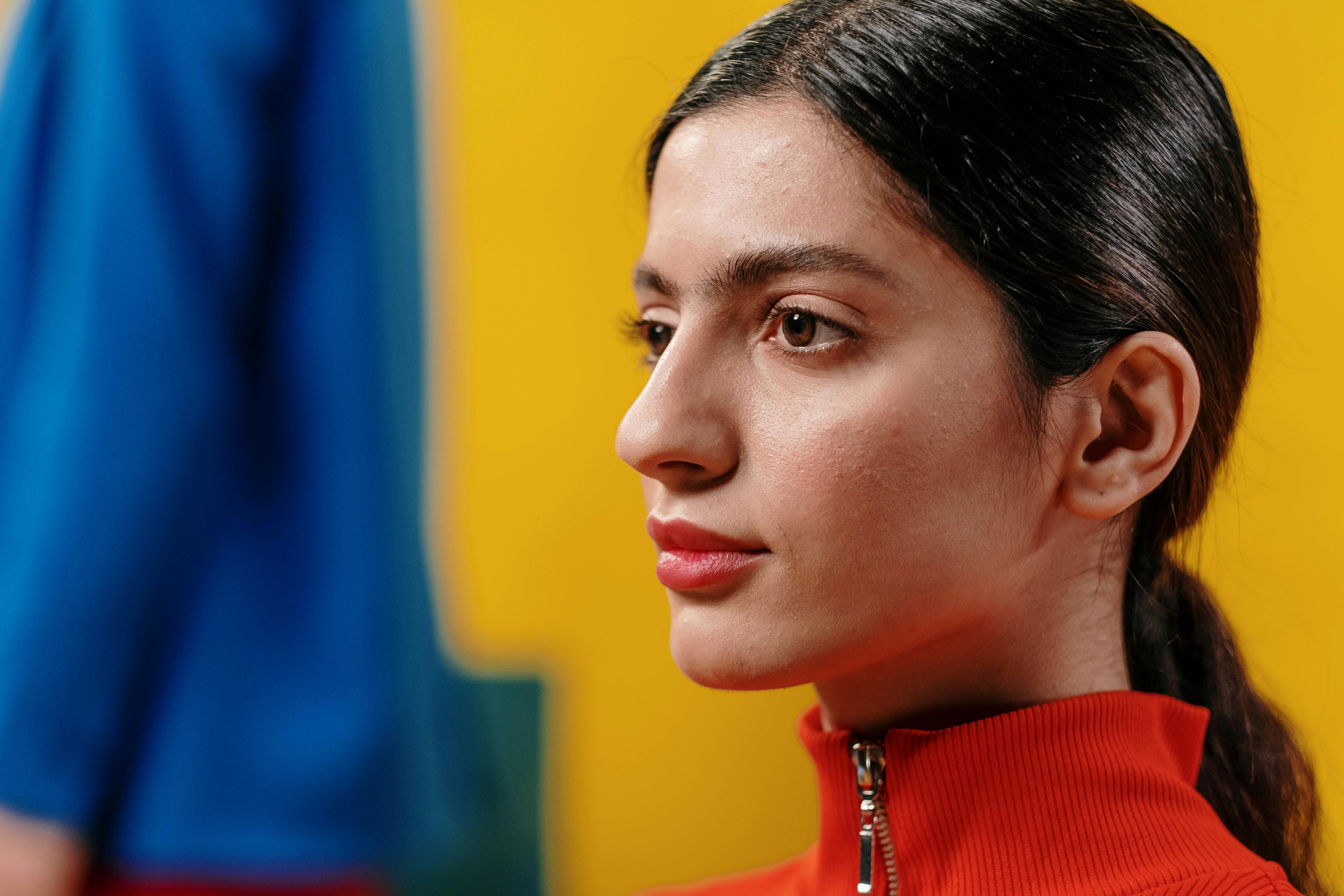 Artistic side profile portrait of a woman in a red turtleneck against a bright yellow backdrop.