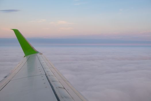 A serene view from an airplane window overlooking a sea of clouds at sunset with a green wingtip.