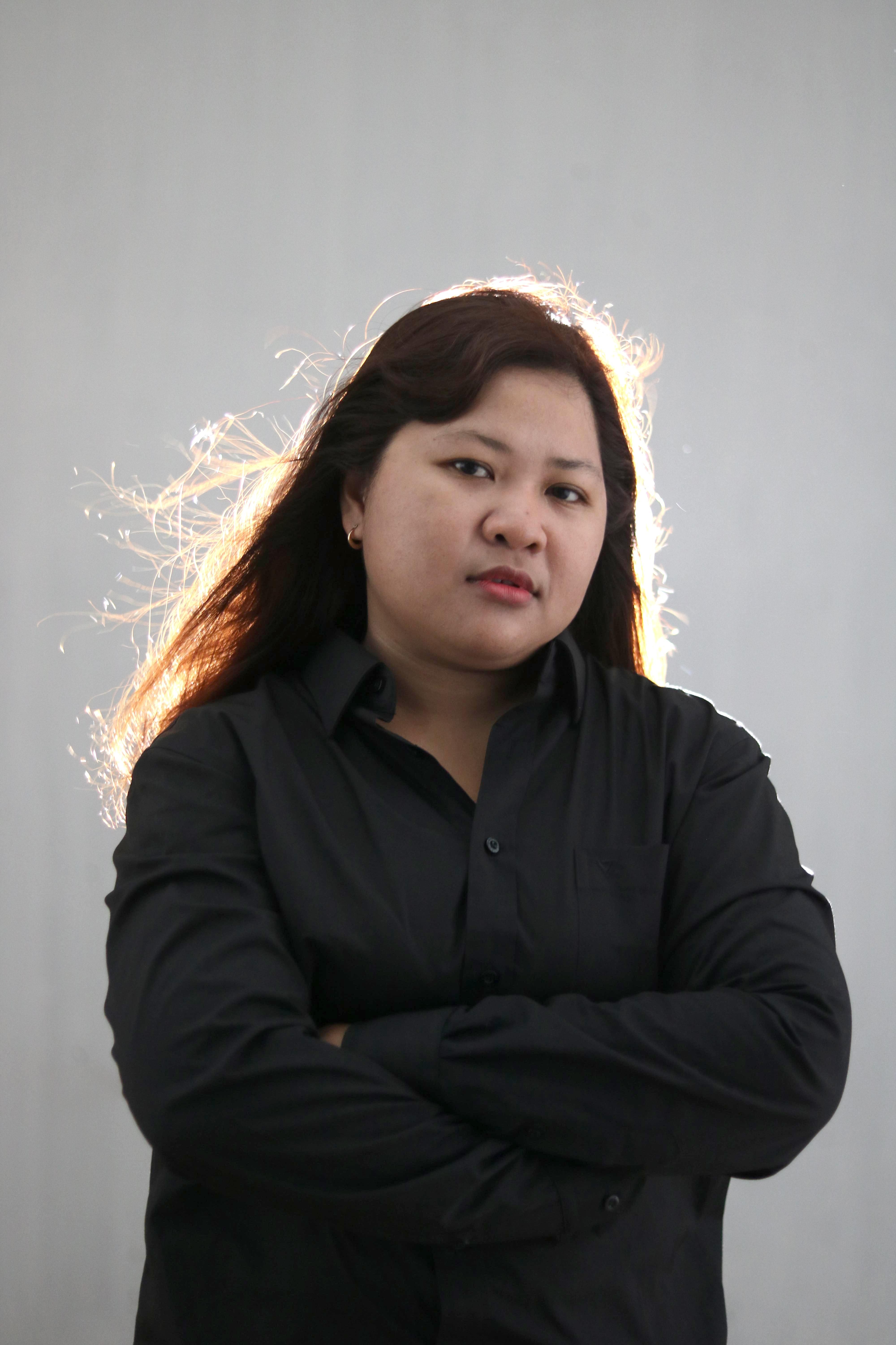 Calm plump Asian female in black wear with dark hair looking at camera while standing on street with crossed arms against gray background