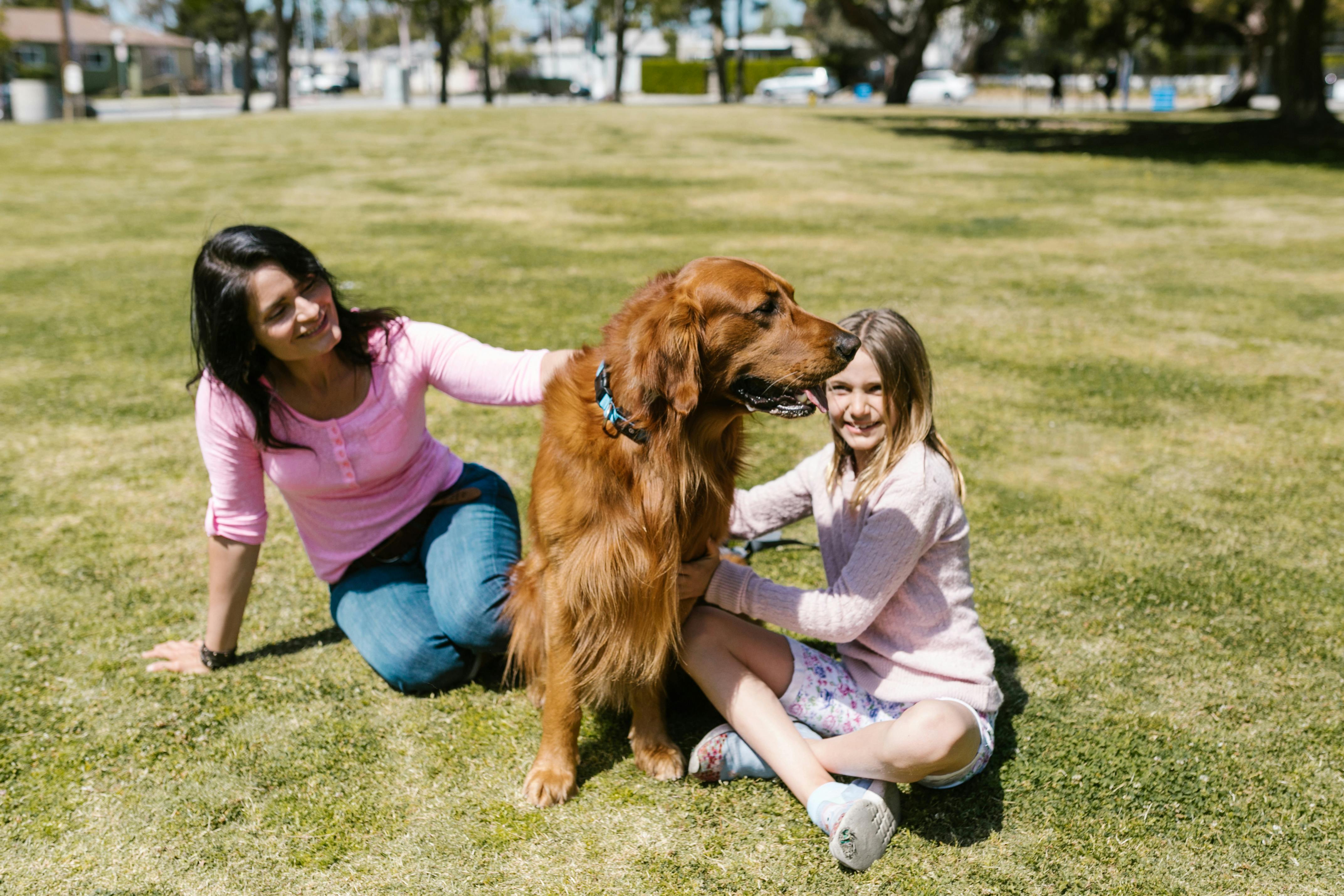 woman and a girl sitting on grass with a dog