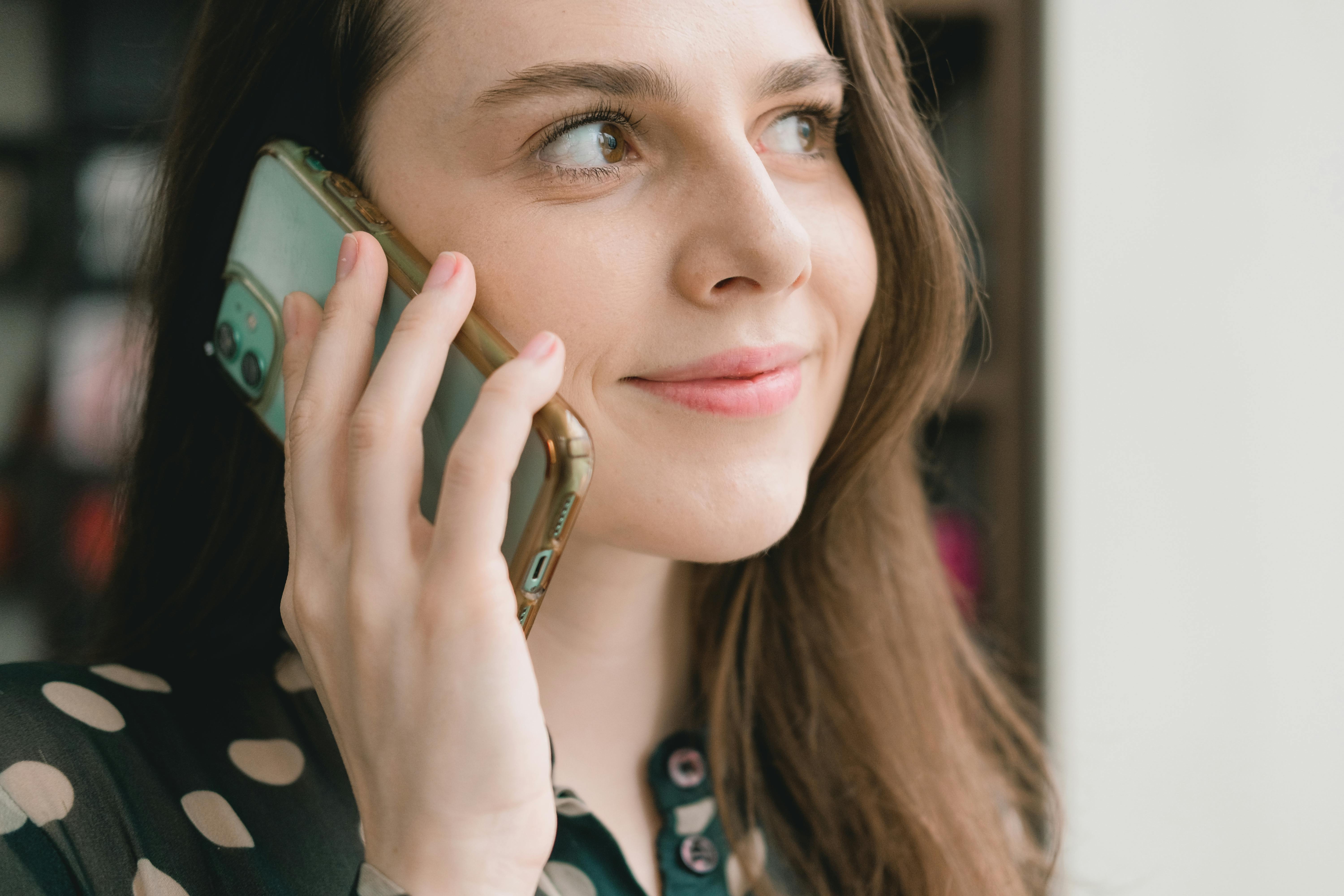 smiling young woman talking on smartphone near window