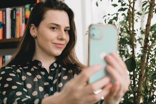 Free Content young woman taking selfie on smartphone near bookshelf Stock Photo
