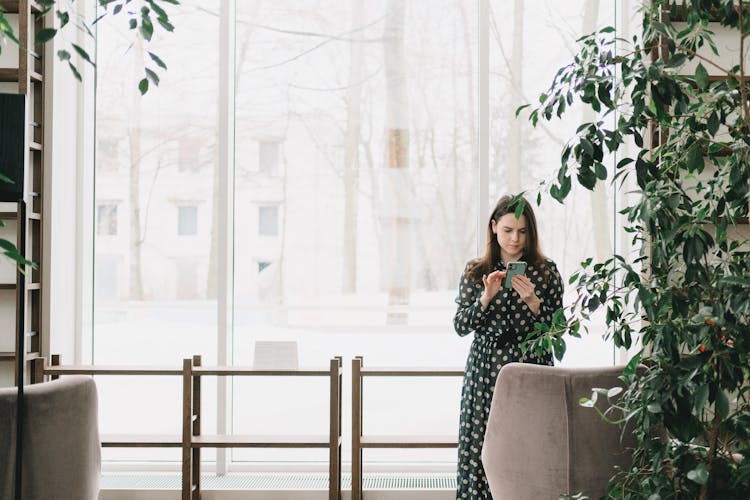 Focused Young Woman Using Smartphone Near Window In Office