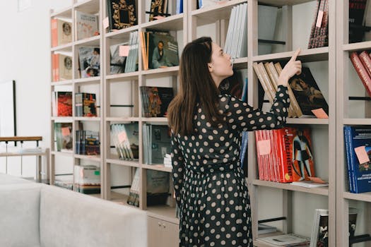 A woman in a polka-dot dress choosing a book from a library bookshelf.