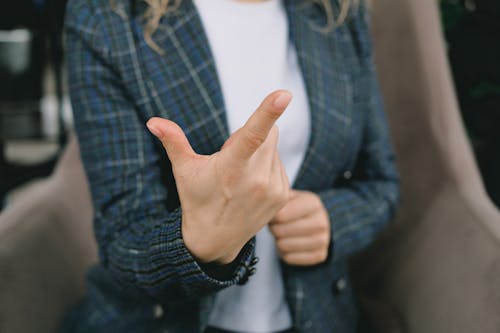 Crop anonymous lady in elegant blazers sitting in comfortable armchair and showing index finger while communicating using sign language