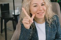 Positive lady gesturing and smiling at camera sitting in armchair