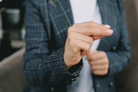 Crop faceless lady in classy blazer showing fingers sign to camera while sitting in armchair and practicing nonverbal communication