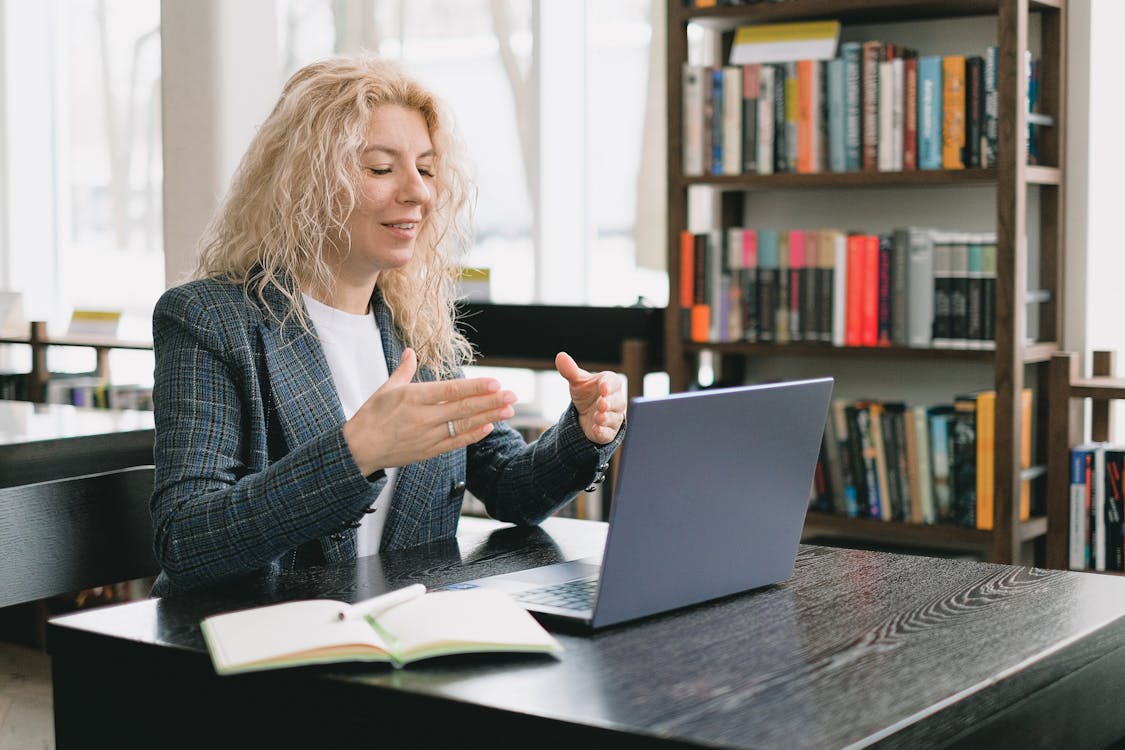 Free Smiling woman having video chat via laptop in library Stock Photo