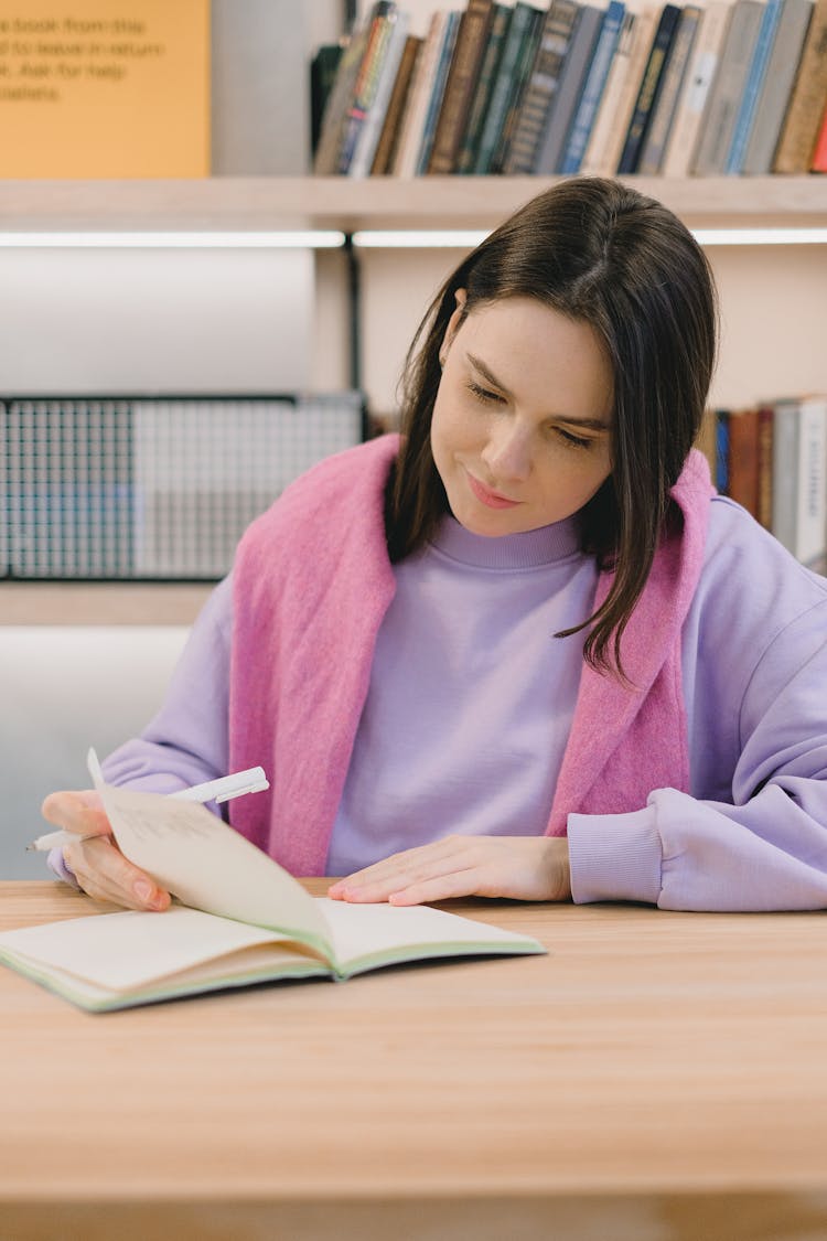 Thoughtful Female Student Reading Notes In Copybook In Classroom