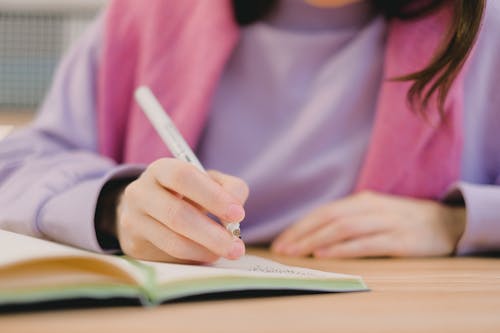 Free Faceless female student writing in notebook during lesson Stock Photo