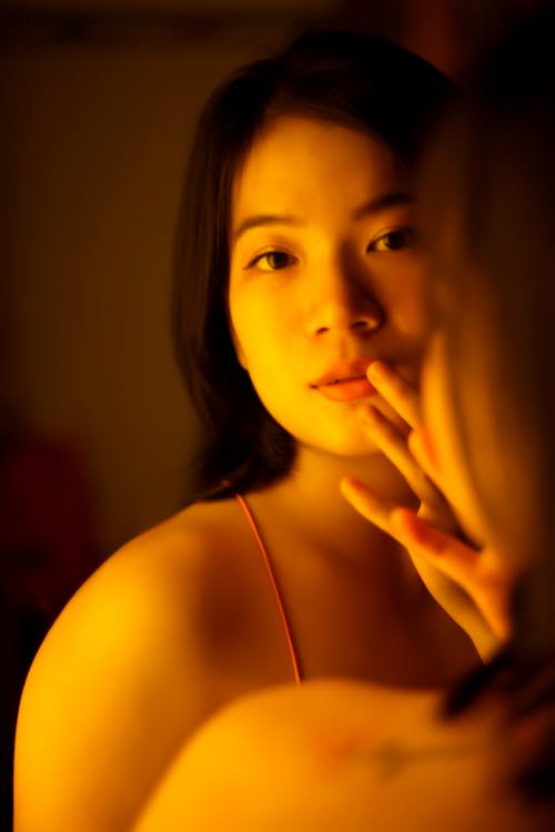 Gentle Asian woman looking at mirror in yellow light