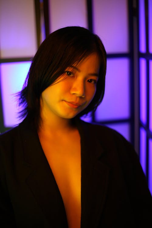 Delicate ethnic alluring female with short hairstyle looking at camera near violet light in studio