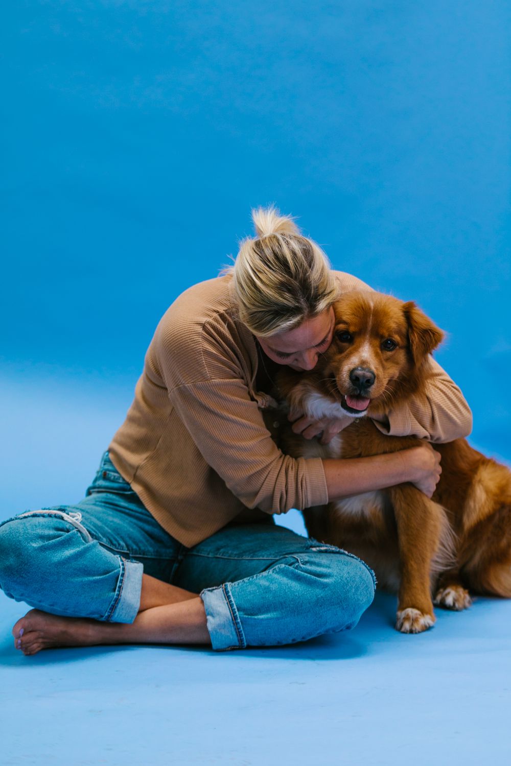 A woman warmly hugging her dog against a blue studio background