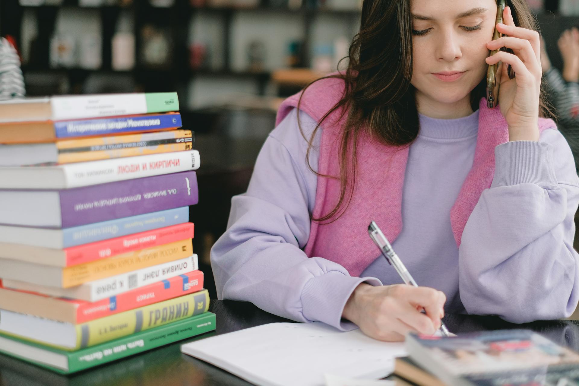 Woman multitasking with books and phone call in library setting.