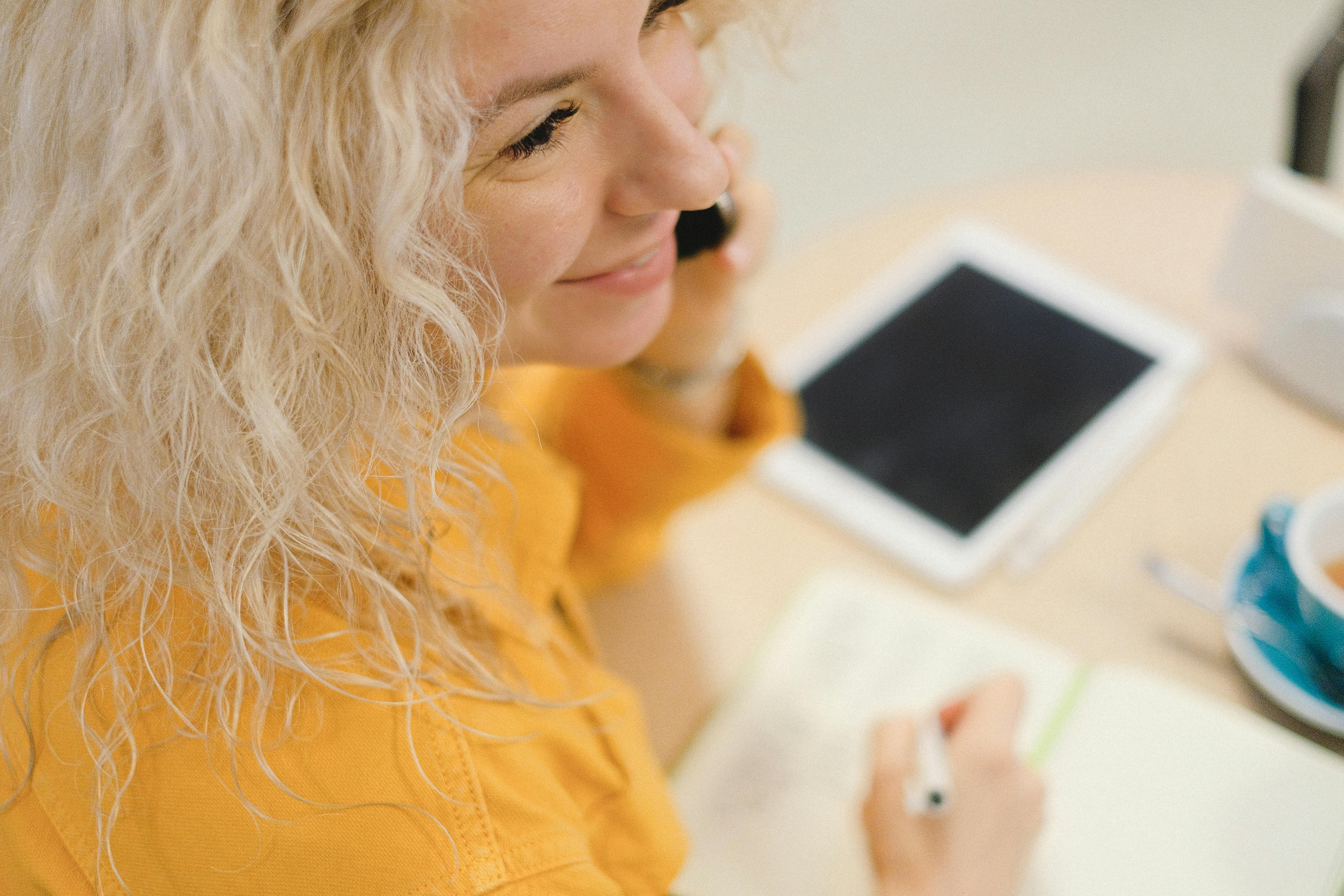 woman with smartphone and cup writing notes during distance work