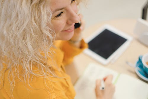 Woman with smartphone and cup writing notes during distance work