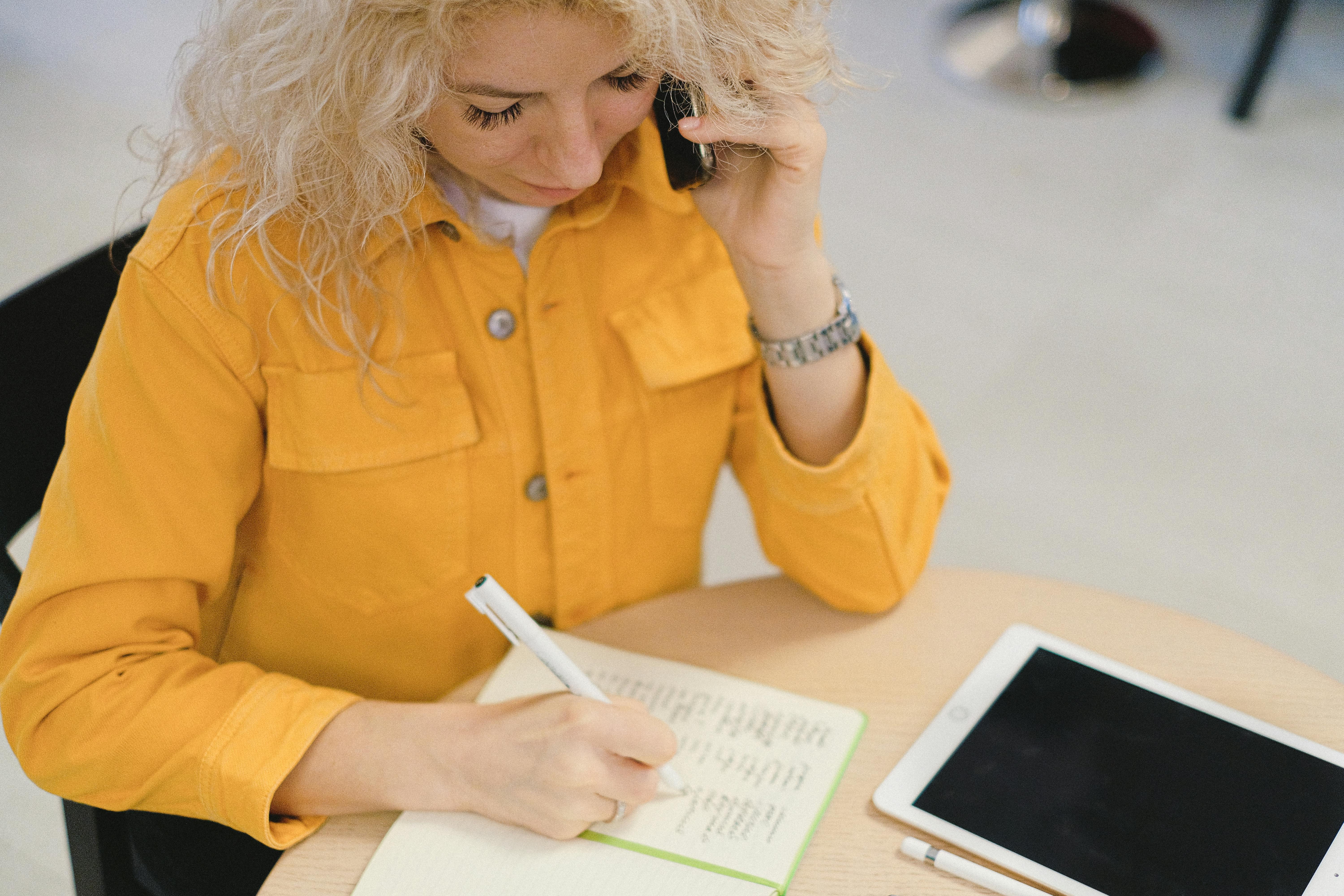 woman writing in planner during business call