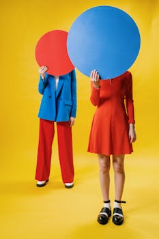 Two people in vibrant outfits holding large colored circles on a yellow background.