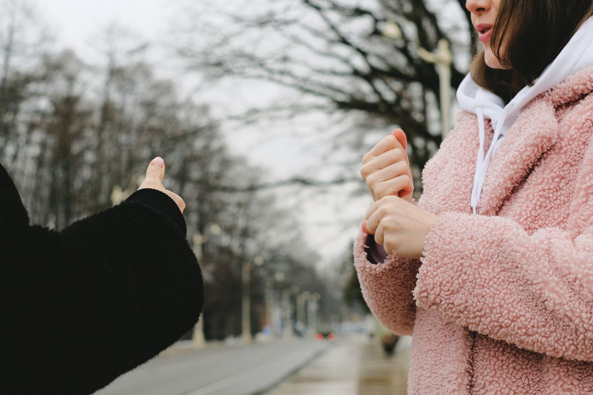 Two women communicating using sign language on a winter street, capturing a candid moment of connection.