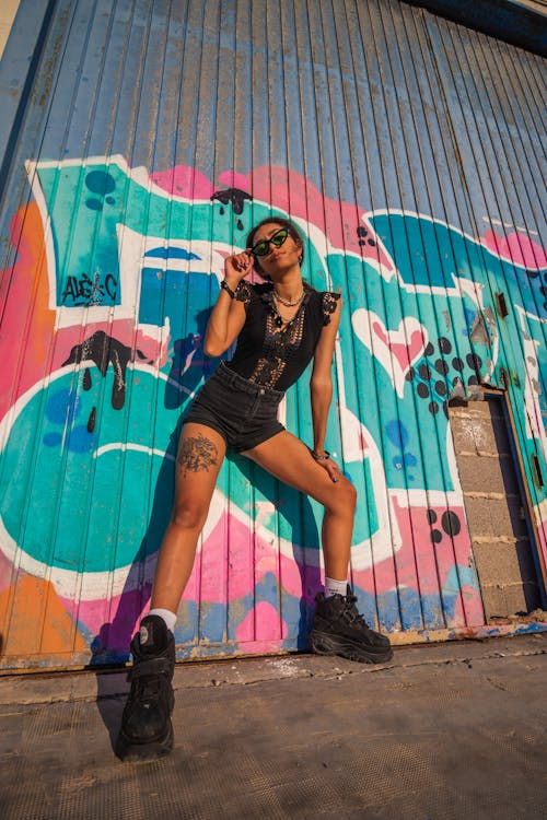 Low-Angle Shot of a Woman with Black Shoes Posing Near a Graffiti Wall