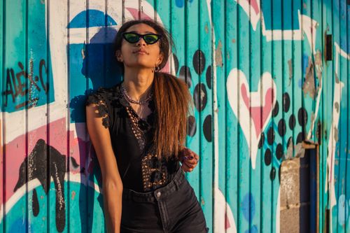Free Trendy woman with sunglasses leans against a colorful graffiti wall in Valencia. Bold and artistic vibe. Stock Photo