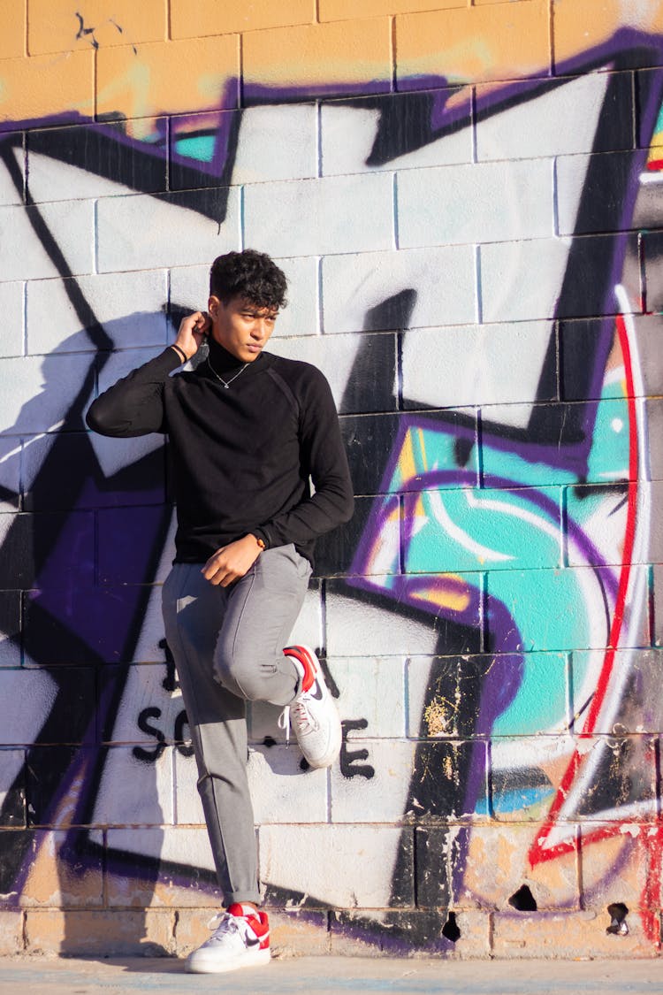 Man In Turtleneck Shirt Leaning On A Wall With Graffiti