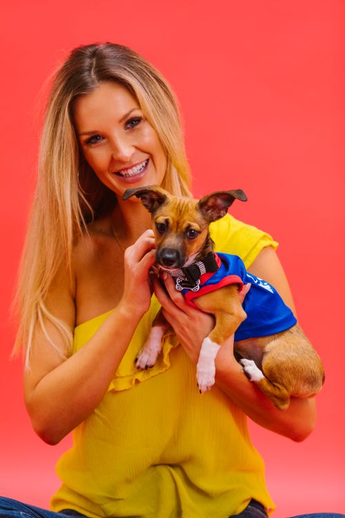 Free Cheerful woman in yellow top holding a cute dog against a vibrant pink background. Stock Photo