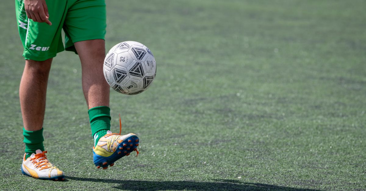 A football (soccer) player juggling a ball on a field with a beautiful orange sunset behind them