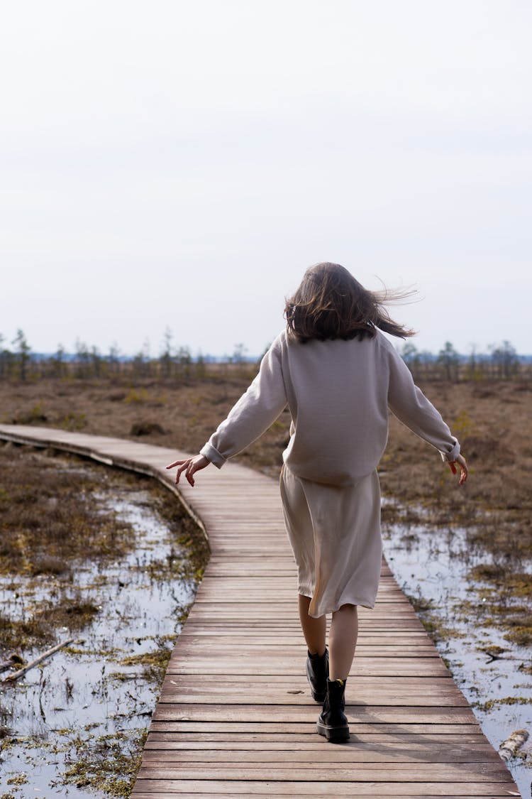 Woman Walking On Wooden Path In Windy Weather In Spring