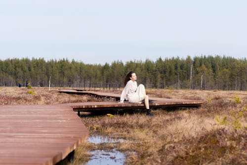 Woman relaxing on long wooden path among grass