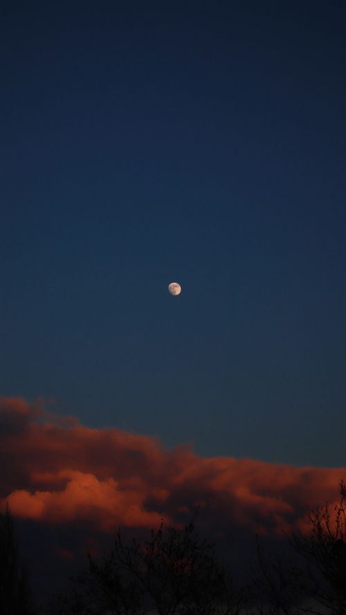 Free A serene moonlit sky with clouds illuminated by the warm colors of sunset, creating a dramatic natural scene. Stock Photo