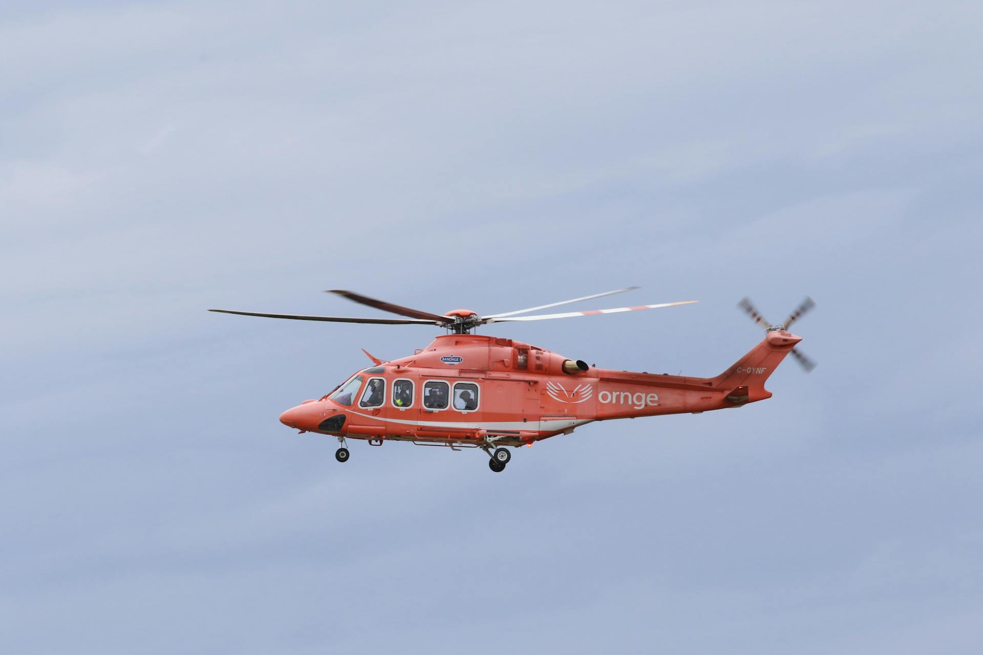 Orange rescue helicopter flying in clear sky, showcasing aviation detail and medical transport theme.