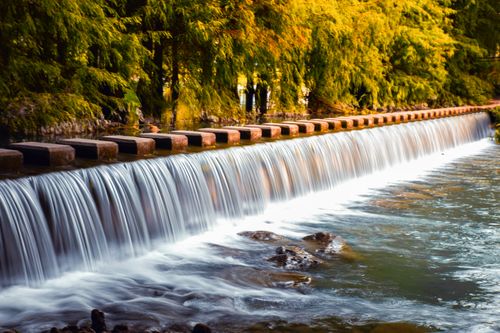 Free Tranquil waterfall cascading over rocks in a verdant forest with vibrant foliage. Stock Photo