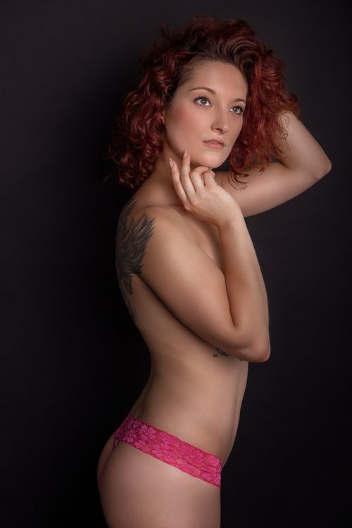 Free Studio portrait of a redheaded woman posing with a tattoo on black background. Stock Photo