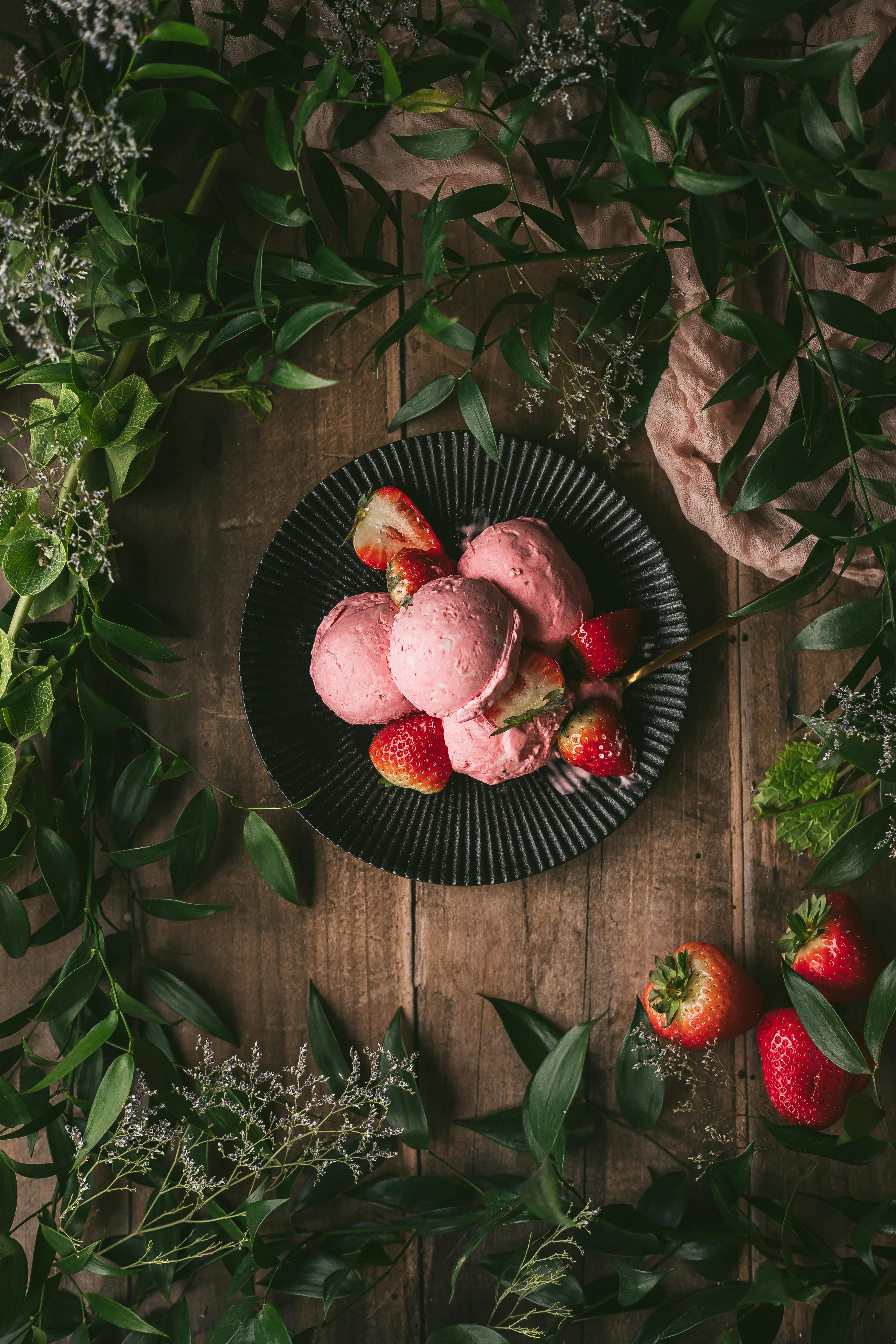 A top view of strawberry ice cream with fresh strawberries surrounded by green leaves and wooden texture.
