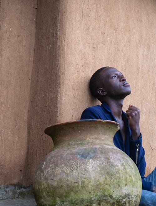 A Man Leaning on the Wall and Sitting Beside the Pot