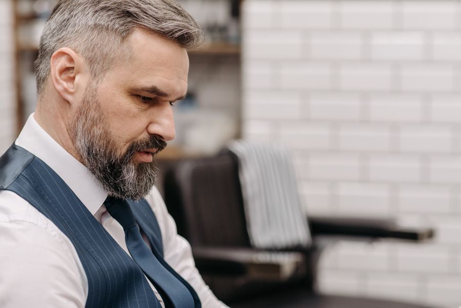A bearded man in a waistcoat looking down in profile
