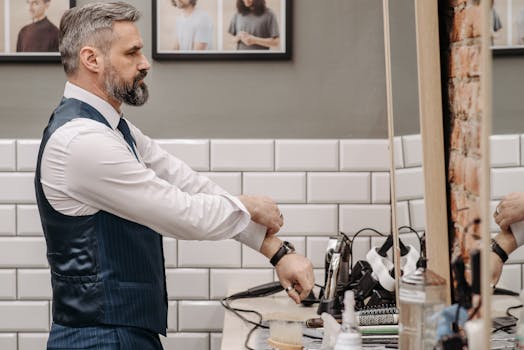 A bearded man in corporate attire adjusts his shirt in a barbershop, captured in a reflective moment.